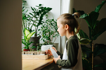 Side view of a boy standing next to a window sill, holding a spray bottle
