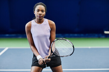Front view portrait of young black sportswoman playing tennis at indoor court, copy space