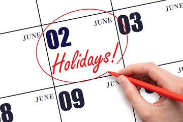 Hand drawing a red circle and writing the text Holidays on the calendar date 2 June. Important date.