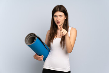 Young Ukrainian sport girl going to yoga classes while holding a mat surprised and pointing front