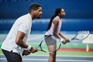 Side view portrait of two young African American people playing tennis at indoor court, copy space