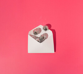 Opened white invitation / letter envelope full of disco balls on pink background. Sharp shadow....