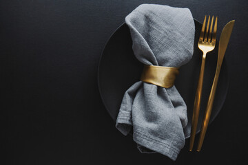 Golden cutlery set with dark plate - obrazy, fototapety, plakaty