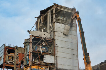 Fototapeta na wymiar Hydraulic scissors destroy abandoned industrial building