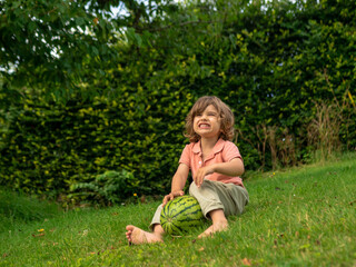 Fototapeta premium A little toddler boy is eating fresh watermelon on a sunny day on his summer holidays at the countryside in a cottage in England