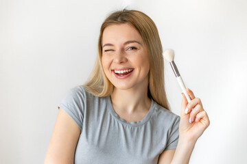Enjoyed smiling adorable makeup artist hold brush near face satisfied and posing isolated on white...