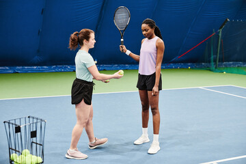 Full length portrait of female tennis coach working with young black woman during practice at...