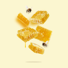 Flying pieces of honeycomb, drop of honey and bees on a yellow background. A conceptual composition...