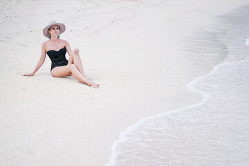Vacation on the seashore.Young woman in hat and swimsuit relaxing on the white sand beach.