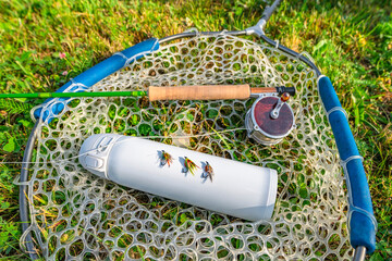 Fly fishing tackle. Flies on thermo water bottle, rod, reel in fishing landing net