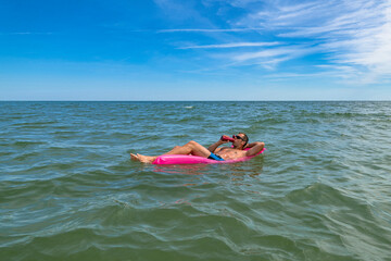 Tanned man relax on pink inflatable mattress at sea. Successful Guy in sunglasses enjoying vacation...