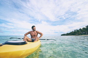 Young strong man kayaking in the sea near the tropical island. Adventure by kayak.