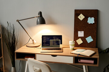 Background image of cozy home office workplace with code on laptop screen lit by lamplight, copy space