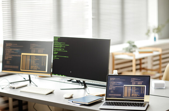 Background image of IT developers office with code on computer screens and devices