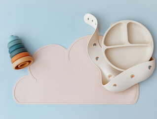 Set of silicone dishware and baby accessories on blue light background, flat lay