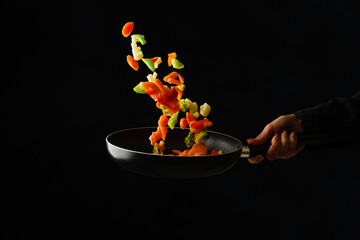 Shrimps with vegetables in a frying pan on a black background. Seafood in frozen flight. Organic...