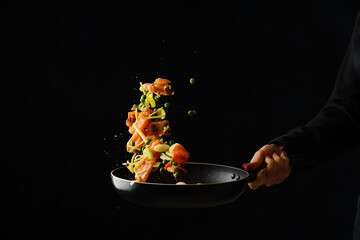 Sea food delicacies. Assorted seafood and vegetables in a frying pan in the hand of a professional chef. Food on a black background. Levitation. Seafood recipes for real gourmets.