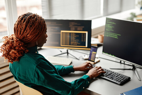 Side view of female IT developer typing on keyboard with programming code on computer screen while working in office interior, copy space