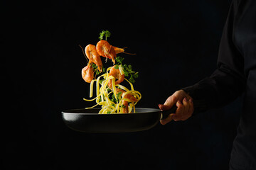 Shrimps with pasta and vegetables in a pan in a frozen flight on a black background. Sea food. Healthy vegetarian food. Organic gourmet food. Banner, advertisement, invitation.