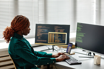 Side view of African American IT developer typing on keyboard with programming code on computer...