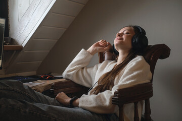 Young woman listening to music in big headphones near computer at home. Creating play list, enjoying free or working time. Female at her 20s near desktop. Copy space