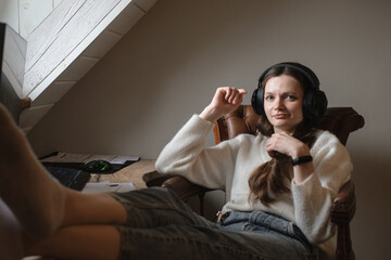 Obraz premium Young woman listening to music in big headphones near computer at home. Creating play list, enjoying free or working time. Female at her 20s near desktop. Copy space
