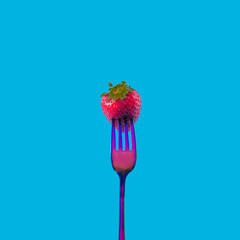 A fresh organic strawberry on a neon colored flashy fork against blue background. Vibrant minimal concept for seasonal fruits banner. Artistic design for contemporary neon trend