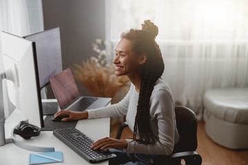 Smiled cheerful female web expert sitting at desk in living room coding on computer
