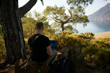Man inspiring for a work inside the mountains. Sitting on the rock and working online. High quality photo