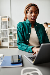 Vertical portrait of black young woman using laptop while working at desk in software development...