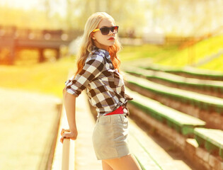 Portrait of beautiful young blonde woman wearing shorts, shirt in summer park