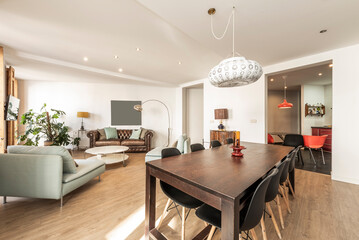 Living room with dark wood dining table with black resin and wood chairs, brown leather chesterfield sofa and light fabric diva