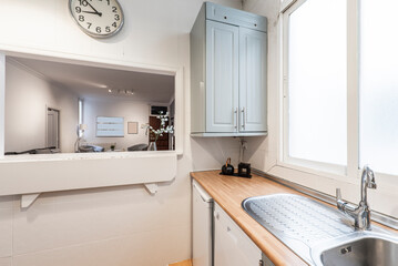 Fototapeta na wymiar kitchen with light wood countertop stainless steel sink under window and white framed serving hatch