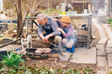 granddaughter helps grandfather with dog cook barbecue on the grill, bonfire