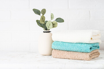 Stack of bath towels and vase with green plant. Clean towels in the laundry or bathroom. White background.