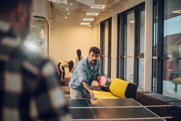 Young people playing table tennis in the office at work