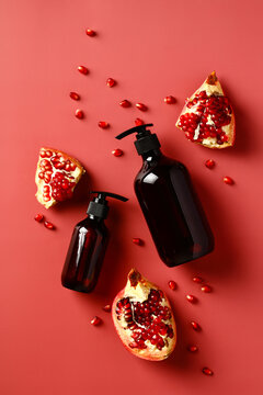 Pomegranate shower gel and shampoo bottles with slices of garnet and seeds on red background. Pomegranate SPA cosmetics design.