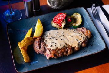 Grilled beef steak with cream sauce with potatoes, peppers and sliced zucchini on a platter