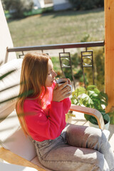 Young woman enjoying the view from apartment,drinking morning coffee on the balcony.