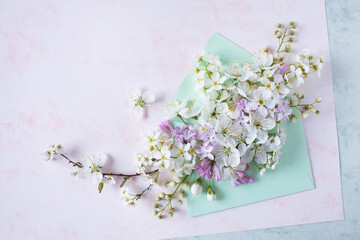 Bouquet of bird cherry flowers, spirea, lilacs, white fruit flowers in an envelope on white-pink decorative paper and space for text. Greeting card for the holiday.