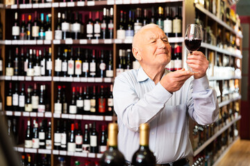 Elderly man checks the color and taste of red wine in a liquor store. High quality photo