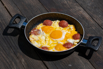Selective focus closeup shot of fried eggs in frying pan on wooden table.