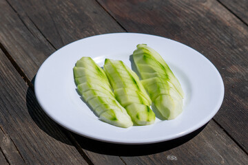 Selective focus down view of plate of sliced cucumbers on wooden table.
