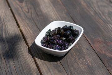Selective focus down view of plate of black olives on wooden table.