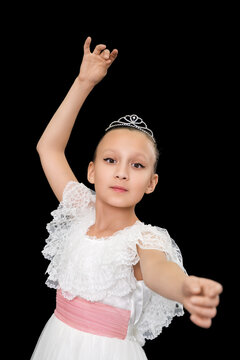 Cute girl ballerina in white long dress dancing on black background. Caucasian ballet dancer nine-year-old posing and looking at camera. Waist up, studio shot. Part of photo series