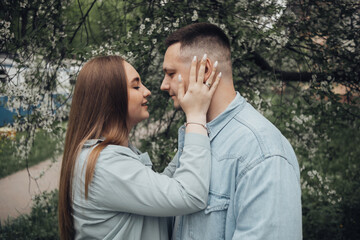 a guy and a girl stand against the background of a flowering tree and are going to kiss