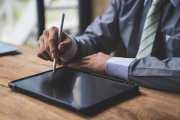 Man working contemporary electronic tablet while sitting at the wooden table at office.Men using...