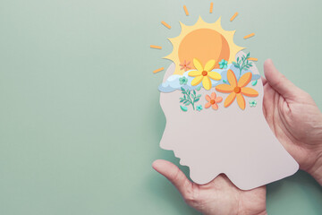 Hands holding paper brain with flowers and sunshine, positive mental health, happy mood, self care concept - obrazy, fototapety, plakaty