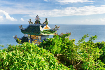 Tile roof of Buddhist temple among foliage on sea background