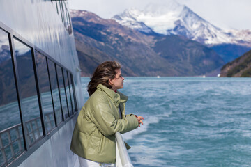 A girl on board a tourist boat admires the views of the lake and mountains on a sunny cold day, Argentina, El Calafate.